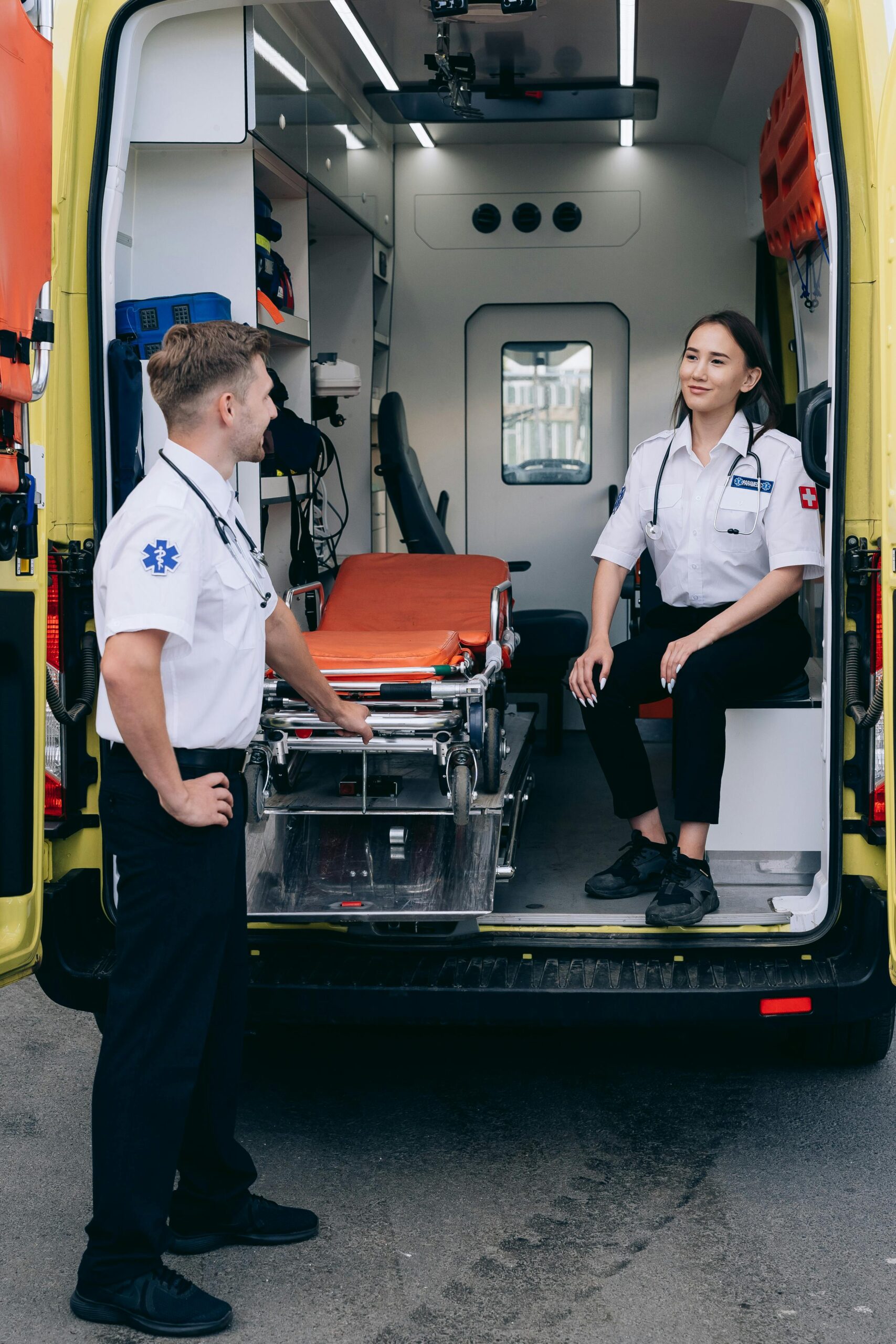 Two paramedics in uniforms conversing inside an ambulance with medical equipment.